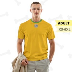 May include: A yellow t-shirt with a green collar and the word "PLUTO" on a circular emblem. The shirt is labeled "ADULT" and available in sizes XS-6XL. The person is holding a tan jacket.