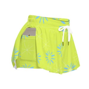 May include: Lime green athletic skirt with a white drawstring and a pocket. The skirt features a pattern of blue and white starburst designs. A smartphone is visible in the pocket.