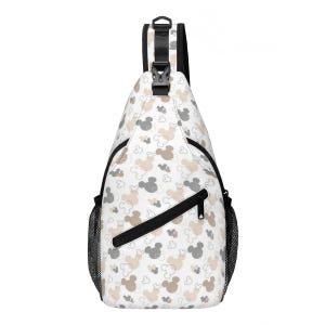 May include: White sling bag with a pattern of Mickey Mouse heads in gray and tan. The bag has a black zipper, black mesh side pocket, and a black strap. The bag is designed to be worn over one shoulder.