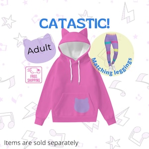 Könnte beinhalten: Rosaer Hoodie für Erwachsene mit einer weißen Kapuze und Katzenohren. Der Hoodie hat eine lila Katzen-Tasche auf der Vorderseite. Der Text "CATASTIC!" ist in blauen Buchstaben über dem Hoodie. Der Text "Adult" ist in lila Buchstaben auf einer lila Katzenkopfform. Der Text "Matching Leggings" ist in blauen Buchstaben auf gelbem Hintergrund.