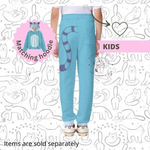 May include: Blue sweatpants with a cat tail design and the text "Hugs and Mugs Creative Designs by Eliza" on the right leg. The sweatpants are paired with a matching blue hooded sweatshirt with cat ears. The text "Matching hoodie" is on a pink circle in the top left corner of the image. The text "KIDS" is on a pink rectangle in the top right corner of the image.