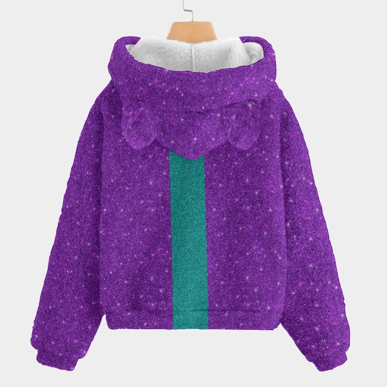 May include: A purple hooded sweatshirt with a glittery texture and a teal stripe down the center. The hood has a white, fluffy lining and small, rounded ear-like details. The sweatshirt is hanging on a wooden hanger.
