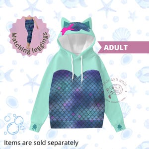May include: A teal and blue mermaid scale hoodie with cat ears and matching leggings. The hoodie features a white drawstring and the word "ADULT" is printed on the image. The text "Items are sold separately" is also visible.