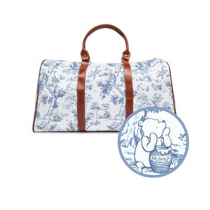 May include: A white and blue toile print travel bag with brown leather handles and a Winnie the Pooh character on the front. The character is holding a honey pot that says "Hunny".