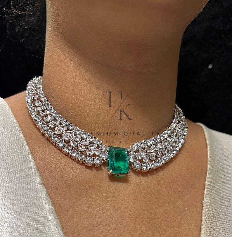 Puede incluir: Un lujoso collar gargantilla con un gran colgante rectangular de esmeralda. El collar est&aacute; adornado con numerosas piedras claras y brillantes. El dise&ntilde;o es elegante y llamativo, perfecto para ocasiones especiales.