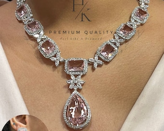 May include: A silver necklace with a pink pear-shaped pendant and matching earrings. The necklace features a row of rectangular pink stones surrounded by smaller clear stones. The text "PREMIUM QUALITY Feel like a Diamond" is visible on the necklace.