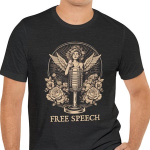May include: A black t-shirt featuring a vintage-style illustration of a woman with wings singing into a microphone. The illustration is surrounded by roses and the text "FREE SPEECH" is printed below.