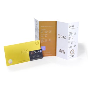 May include: A gold-colored envelope and a small black and white card with the text "GRA" and "GLOBAL GEMOLOGICAL RESEARCH ACADEMIA" are displayed. A white brochure with the GRA logo and text is also visible. The items are on a white background.