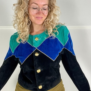 May include: A vintage suede jacket with a colour block design. The jacket features teal, blue, and black panels with gold trim and gold buttons. A unique piece of retro fashion.