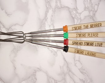 May include: Set of four stainless steel marshmallow roasting sticks with wooden handles. Each handle has a different engraved message: "S'more the merrier", "S'more please", "Spread S'more love", and "S'more laughs".