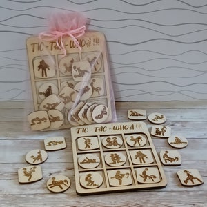 May include: A wooden tic-tac-toe game with a suggestive theme. The game board has 9 squares and the pieces are small wooden figures in various poses. The game is packaged in a pink organza bag with the words "Tic-Tac-Whoa!" printed on it.