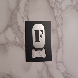 May include: Black bottle opener with a silver letter "F" on the front.