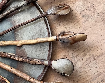 May include: A collection of eight wooden rattles with leather and feather accents. The rattles are arranged in a circle on a metal tray.