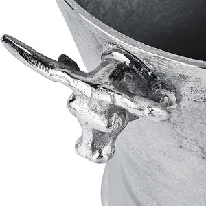 May include: Silver metal ice bucket with a bull head handle. The bucket is round and has a wide opening. The handle is attached to the side of the bucket and has a bull's head design.