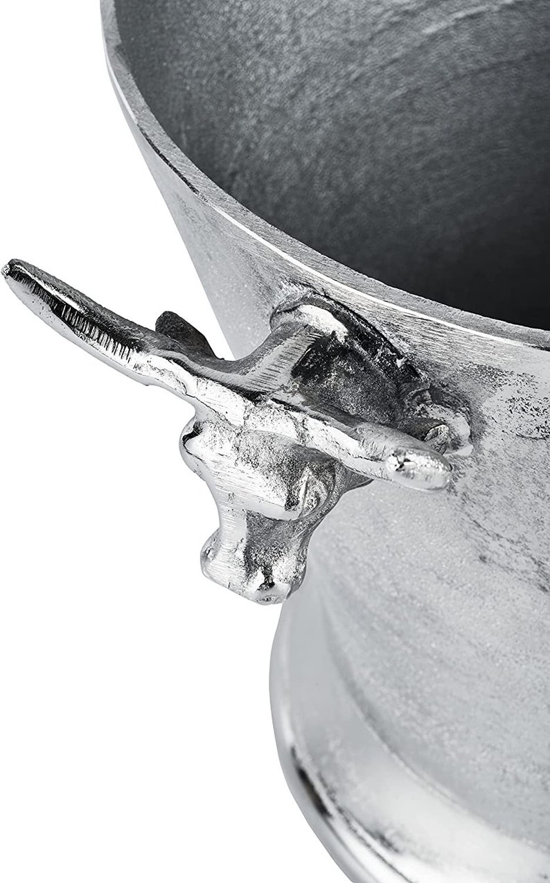May include: Silver metal ice bucket with a bull head handle. The bucket is round and has a wide opening. The handle is attached to the side of the bucket and has a bull's head design.