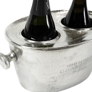 May include: Silver champagne bucket with two bottle holders. The bucket has a handle and the text "...Cuv&eacute;e de Prestige Champagne" is engraved on the side.