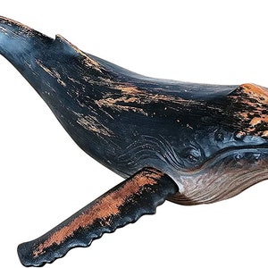 May include: A wooden whale sculpture with a black and brown distressed paint finish. The whale is in a swimming position with its tail and fin raised.