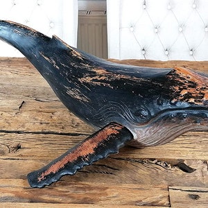 May include: A wooden whale sculpture with a black and orange paint finish. The whale is in a leaping pose with its mouth open. The sculpture has a distressed look, with some of the paint chipped away.