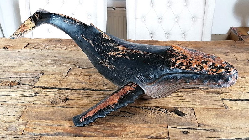 May include: A wooden whale sculpture with a black and orange paint finish. The whale is in a leaping pose with its mouth open. The sculpture has a distressed look, with some of the paint chipped away.