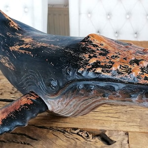 May include: A black and brown whale sculpture with a distressed finish. The whale is carved with details and has a textured surface.