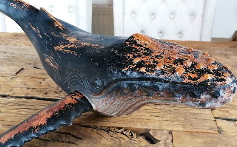 May include: A black and brown whale sculpture with a distressed finish. The whale is carved with details and has a textured surface.