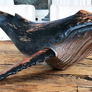 May include: A wooden whale sculpture with a black and brown paint finish. The whale is in a swimming position with its tail raised.