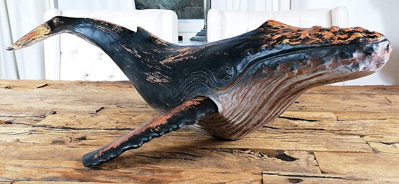 May include: A wooden whale sculpture with a black and brown paint finish. The whale is in a swimming position with its tail raised.