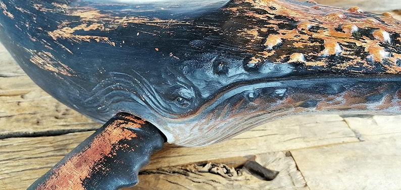 May include: A black and copper whale sculpture with a distressed finish. The whale has a carved design on its body and a tail fin.