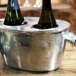 Könnte beinhalten: Silberner Eiseimer aus Metall mit zwei Griffen und zwei Öffnungen für Flaschen. Der Eimer trägt die Aufschrift "Cunning Vintage Champagne".
