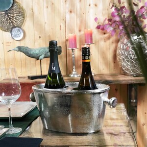 May include: Two bottles of wine in a silver ice bucket on a wooden table with two wine glasses and a decorative whale sculpture.