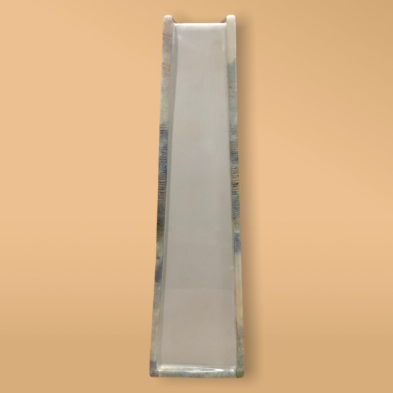 May include: A white plastic slide with a blue and gray patterned design. The slide is tall and narrow, and it is designed for children to play on.