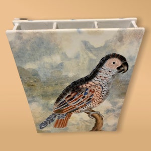 May include: A white ceramic vase with a watercolor design of a parrot perched on a branch. The vase has three compartments for flowers or other decorative items.