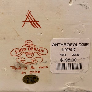 May include: A white ceramic box with a red and black label that reads "John Derian New York" and "Peint a la main en Chine." The label also has a red logo with the letter "A." The box has a price tag that reads "Anthropologie 11997517 4554 29830 $198.00".