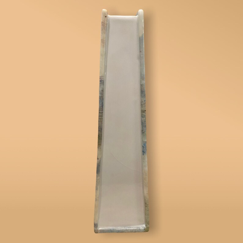 May include: A white plastic slide with a blue and green patterned design. The slide is designed for children's play.