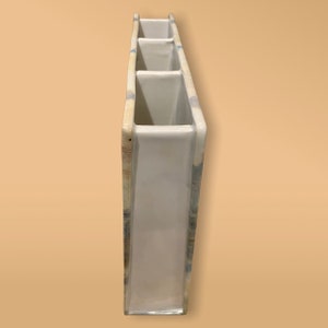 May include: White ceramic vase with four rectangular openings. The vase has a light blue and brown patterned design.