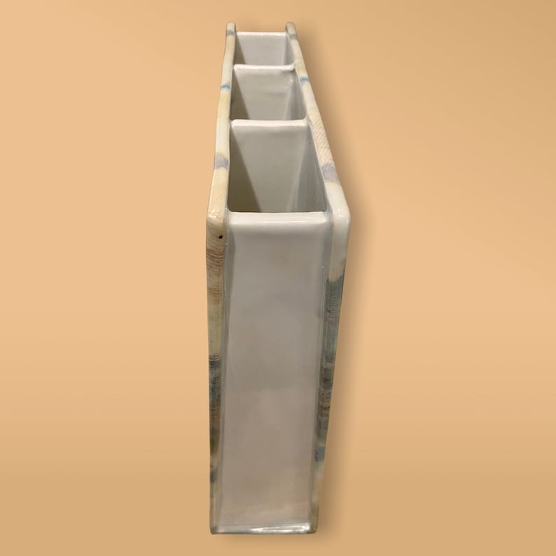 May include: White ceramic vase with four rectangular openings. The vase has a light blue and brown patterned design.