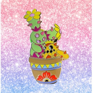 May include: A metal enamel pin featuring a green cactus with pink spikes and yellow flowers, alongside a yellow and orange creature with black spots, both sitting in a brown pot decorated with blue triangles and a large red flower design.