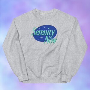 May include: A gray long-sleeved sweatshirt with the text "Serenity Now" in a blue and green oval with a space-themed design.