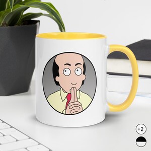 May include: A white ceramic mug with a bright yellow interior and handle. The front features a circular graphic of a cartoon character with a receding hairline, wearing a yellow shirt and red tie, with hands pressed together in a thoughtful gesture.