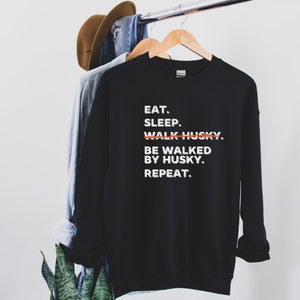 May include: Black sweatshirt with white text that reads "EAT. SLEEP. WALK HUSKY. BE WALKED BY HUSKY. REPEAT."