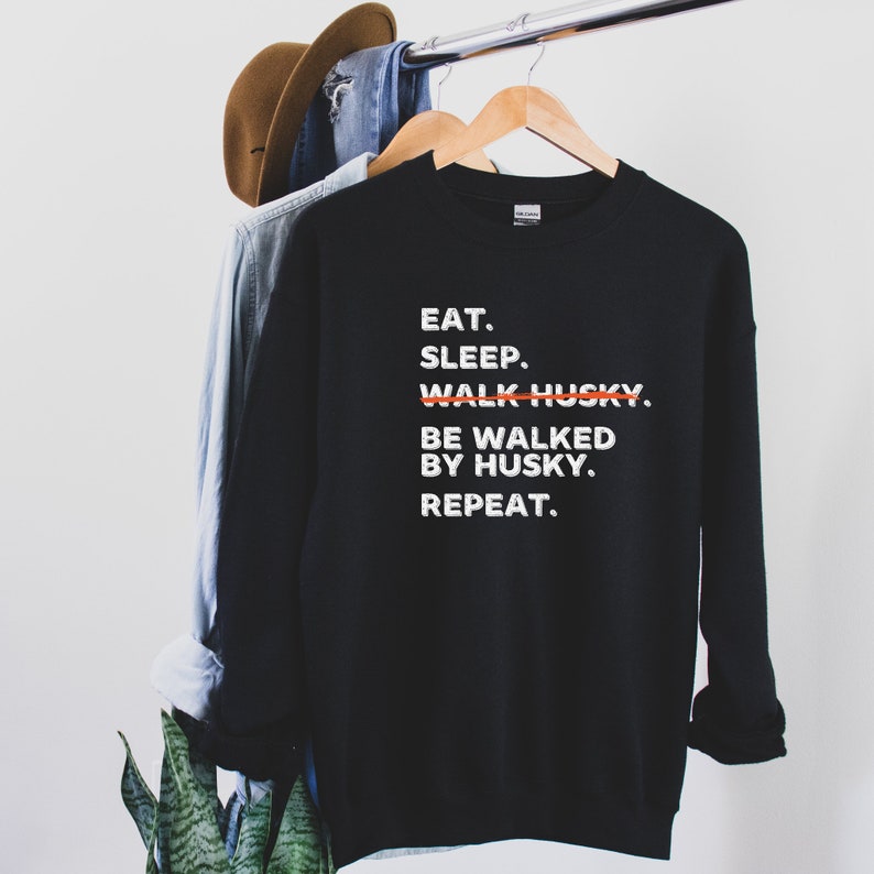 May include: Black sweatshirt with white text that reads "EAT. SLEEP. WALK HUSKY. BE WALKED BY HUSKY. REPEAT."