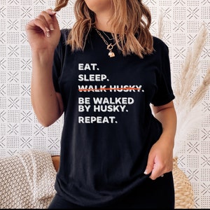 May include: Black t-shirt with white text that reads "Eat. Sleep. Walk Husky. Be Walked By Husky. Repeat."