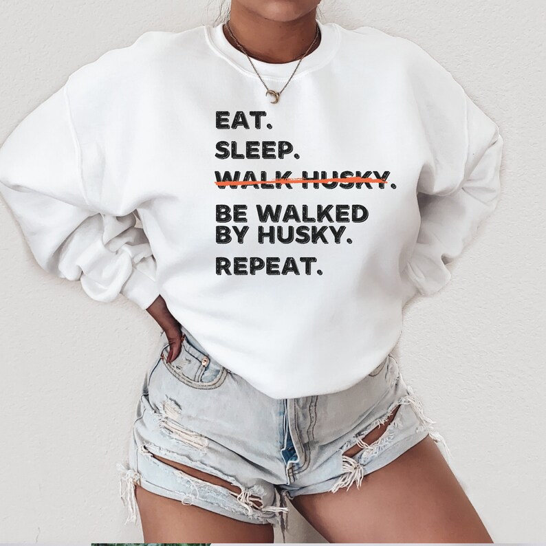May include: White sweatshirt with black text that reads "Eat. Sleep. Walk Husky. Be walked by Husky. Repeat.". The word "Walk" is crossed out with a red line.