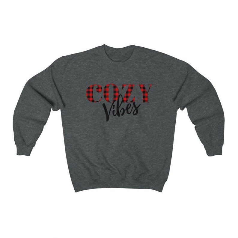 May include: Dark gray sweatshirt with the words "COZY Vibes" printed on the front. The word "COZY" is in a red and black plaid pattern, while "Vibes" is in a black script font. The sweatshirt is a crew neck style.