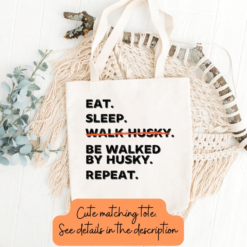 May include: A white canvas tote bag with black text that reads "EAT. SLEEP. WALK HUSKY. BE WALKED BY HUSKY. REPEAT." The text "WALK HUSKY" is crossed out. The tote bag is lying on a white surface with a branch and a macrame piece in the background. The text "Cute matching tote. See details in the description" is written in orange at the bottom of the image.