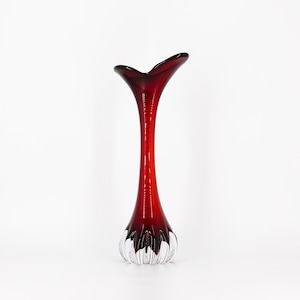 May include: A tall, red glass vase with a unique heart-shaped opening and a clear, textured base.