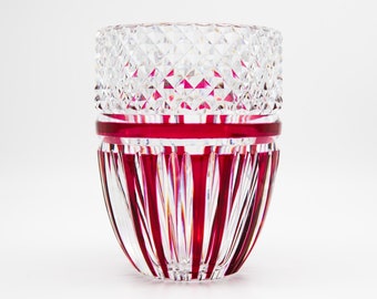 Puede incluir: Un jarrón de vidrio transparente con una banda roja y rayas verticales rojas. El jarrón tiene un patrón de diamante en la parte superior.