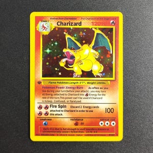 May include: A Charizard Pokémon trading card. The card has a yellow and orange border with a colourful illustration of Charizard. The card text includes the Pokémon's name, stage, and attack details. The card measures 170cm in length and weighs 90kg.