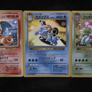 May include: Three Pokémon trading cards featuring Charizard, Blastoise, and Venusaur. The Charizard card shows a red and orange dragon. The Blastoise card depicts a blue turtle. The Venusaur card shows a green plant-like creature.