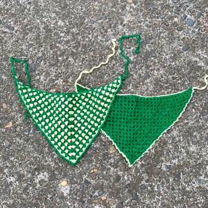 May include: Two crocheted green and white triangle shaped scarves. One scarf is green with white squares and the other is green with white dots.